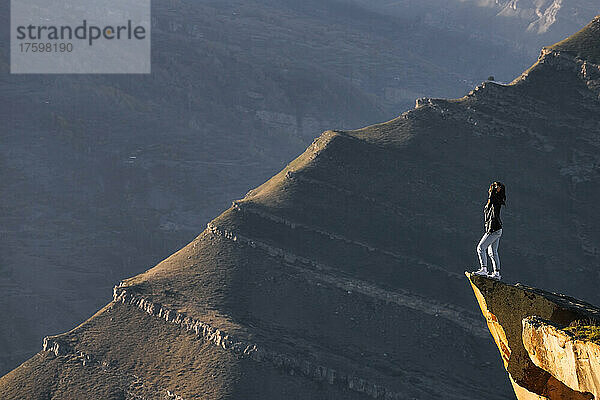 Female hiker admiring landscape of Caucasus Mountains from edge of cliff