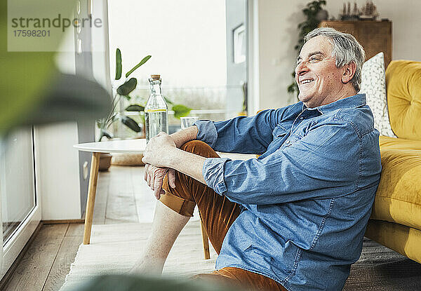 Glücklicher älterer Mann sitzt am Sofa im Wohnzimmer