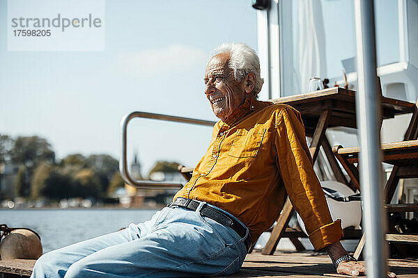 Lächelnder älterer Mann mit weißen Haaren entspannt sich an einem sonnigen Tag auf dem Hausboot
