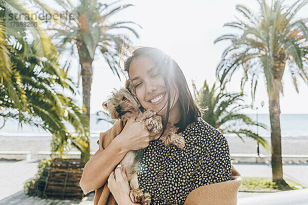 Smiling woman embracing dog at beach on sunny day