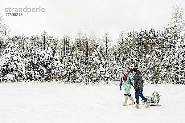 Eltern ziehen Tochter auf Schlitten und laufen im Winter auf Schnee