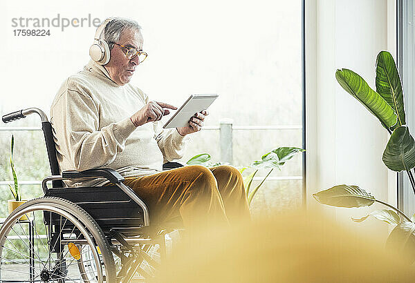 Älterer behinderter Mann benutzt Tablet-PC im Rollstuhl zu Hause