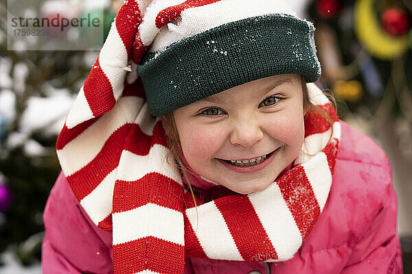 Glückliches süßes Mädchen  das im Winter einen gestreiften Schal trägt