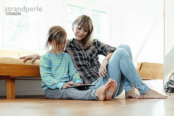 Mutter schaut Sohn mit digitalem Tablet auf dem Boden zu Hause an