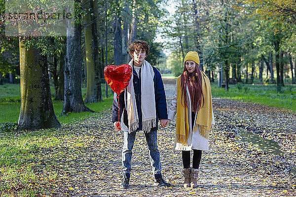 Händchen haltendes Paar steht mit rotem Herzballon im Park