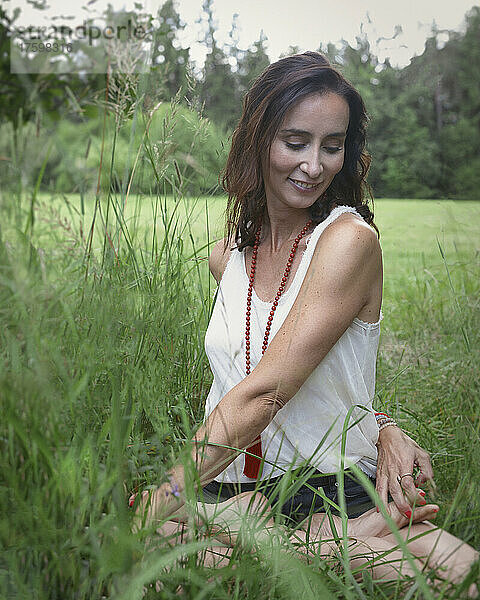 Lächelnde Frau  die Yoga auf Gras in der Natur praktiziert