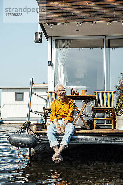 Fröhlicher älterer Mann sitzt am Hausboot und genießt den sonnigen Tag