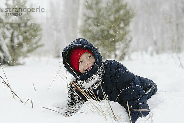 Fröhlicher Junge  der im verschneiten Wald spielt