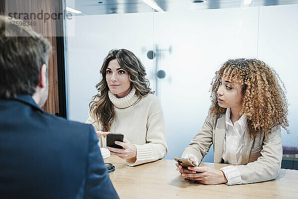 Geschäftsfrauen mit Smartphones unterhalten sich mit einem Geschäftsmann  der am Schreibtisch sitzt
