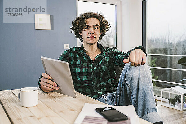 Junger Mann mit Tablet-PC sitzt am Tisch im Wohnzimmer