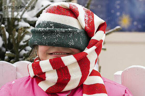 Glückliches Mädchen  das im Winter sein Gesicht mit einer Strickmütze bedeckt