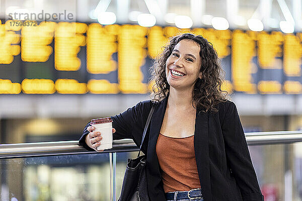 Glückliche junge Frau mit Einwegkaffeetasse am Bahnhof