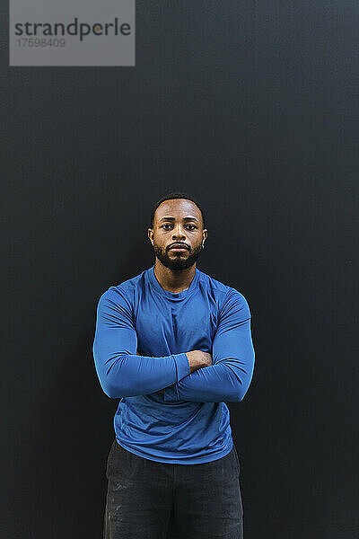 Confident athlete with arms crossed standing against black background