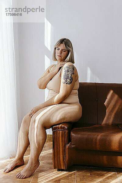 Curvy woman with eyes closed sitting on sofa