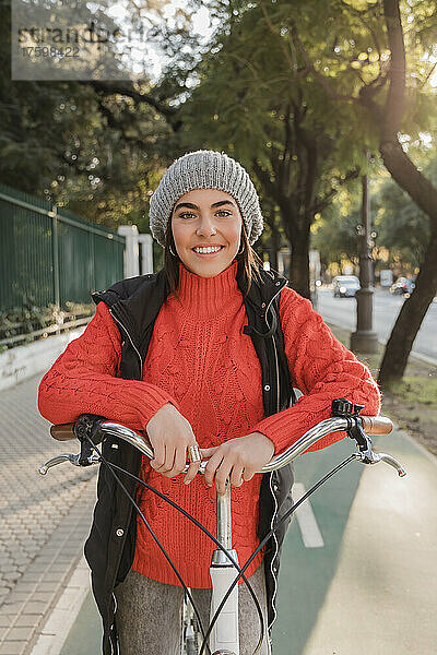 Junge Frau in warmer Kleidung steht mit Fahrrad auf der Straße