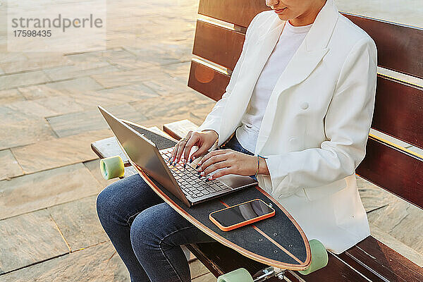 Frau mit Smartphone benutzt Laptop auf Skateboard im Park