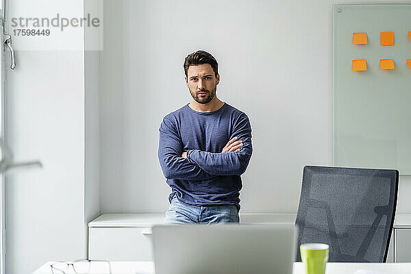 Confident businessman with arms crossed at office