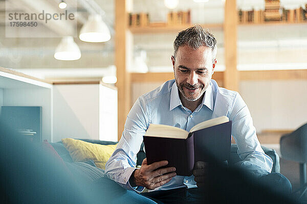 Smiling businessman reading book sitting at workplace