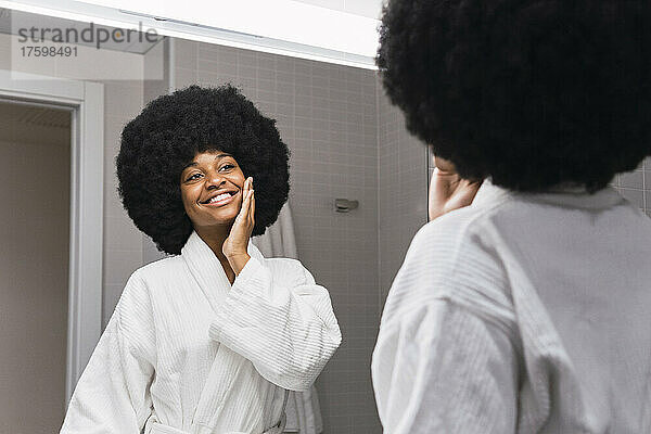 Glückliche Frau  die Hautpflege macht und im Badezimmer in den Spiegel schaut