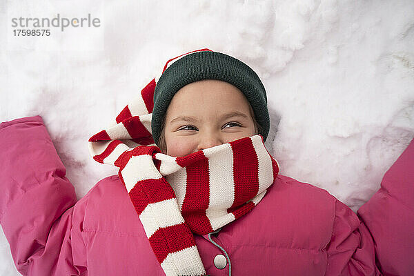 Lächelndes Mädchen mit gestreiftem Schal  das auf Schnee liegt