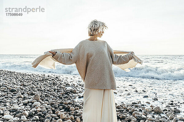Frau mit Decke steht auf Steinen am Strand