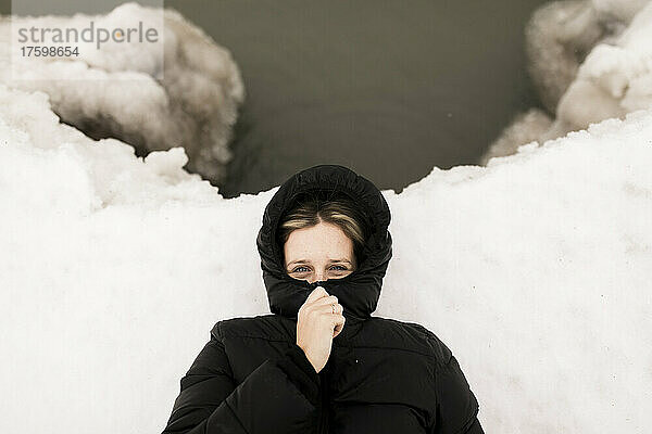 Frau bedeckt Gesicht mit Kapuzenpullover und liegt im Winter im Schnee