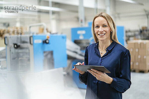 Glückliche Geschäftsfrau mit Tablet-PC steht in der Fabrik