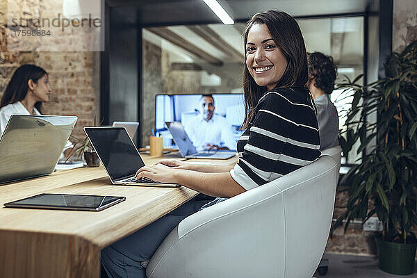 Lächelnde Geschäftsfrau mit Laptop bei Besprechung im Coworking-Büro