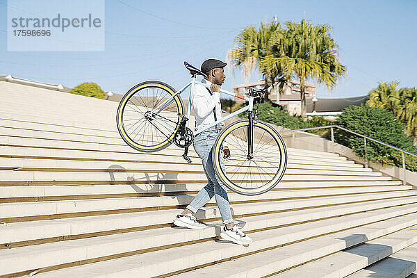 Junger Mann trägt Fahrrad und geht an einem sonnigen Tag die Treppe hinunter