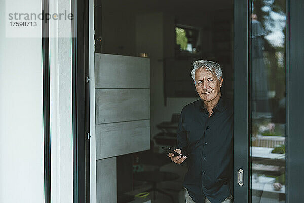 Älterer Mann mit Smartphone steht vor der Tür