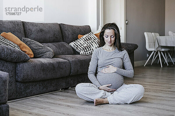 Schwangere Frau sitzt mit gekreuzten Beinen zu Hause