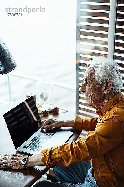 Nachdenklicher älterer Mann mit Laptop sitzt am Tisch im Hausboot