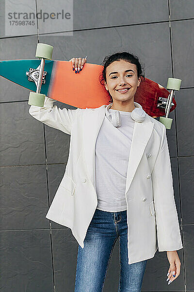 Junge Frau hält Skateboard vor der Wand
