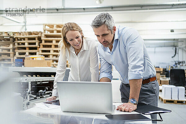 Geschäftsmann und Geschäftsfrau teilen Laptop am Schreibtisch in der Fabrik