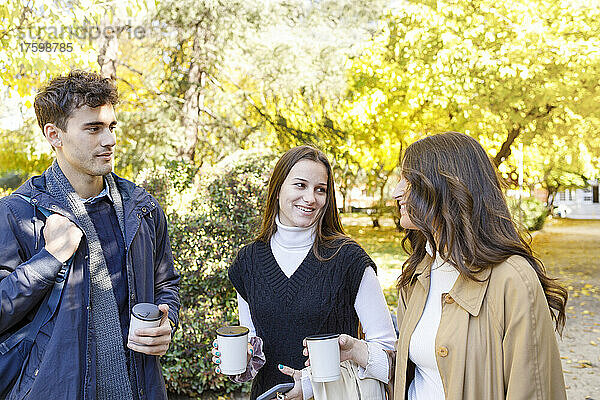 Freunde mit Einweg-Kaffeetasse unterhalten sich im College-Park