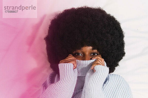 Afro-junge Frau bedeckt Gesicht mit Rollkragenpullover