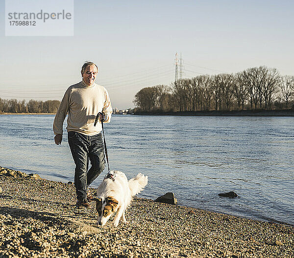 Glücklicher älterer Mann mit Hund  der am Strand spazieren geht