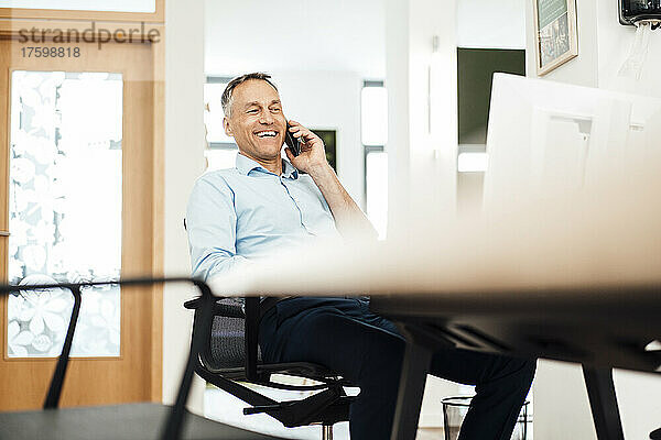 Glücklicher Geschäftsmann  der im Coworking-Büro auf dem Smartphone spricht