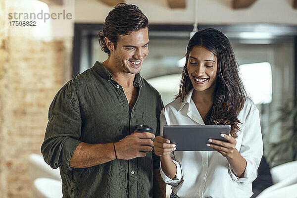 Lächelnde Geschäftsfrau zeigt einem Kollegen im Coworking-Büro einen Tablet-PC