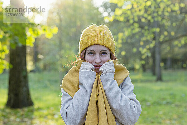 Lächelnde Frau mit gelber Strickmütze und Schal im Herbstpark