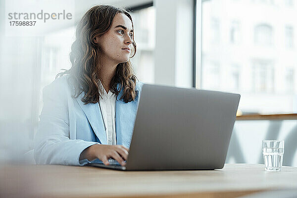Nachdenkliche Geschäftsfrau mit Laptop sitzt am Schreibtisch im Büro