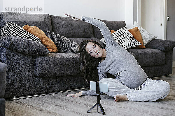 Schwangere Frau trainiert und schaut sich zu Hause Tutorial auf dem Smartphone an