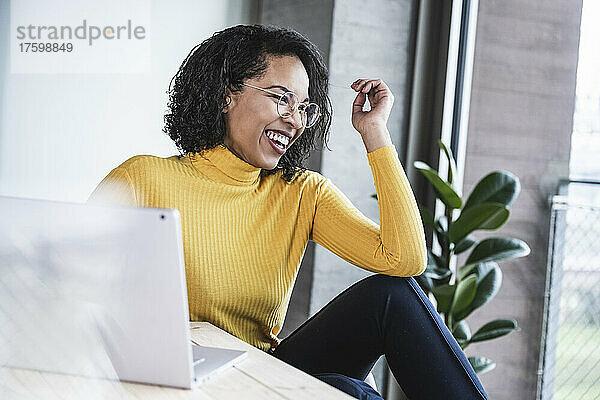 Geschäftsfrau lacht mit Laptop am Schreibtisch im Büro