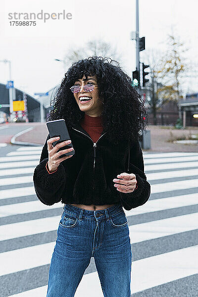 Glückliche junge Frau mit Smartphone steht auf Straßenmarkierung