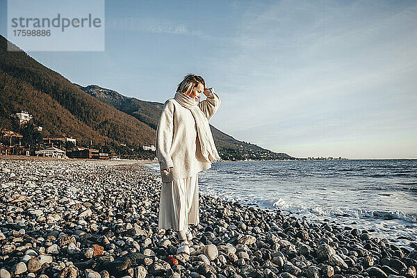 Frau mit der Hand im Haar läuft auf Steinen am Strand