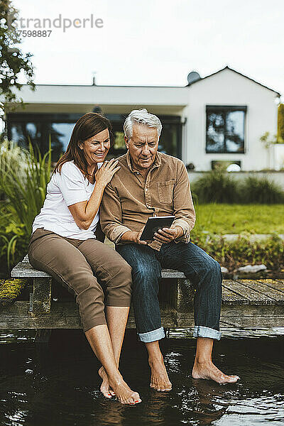 Älterer Mann benutzt Tablet-PC von Frau  die auf dem Steg im Hinterhof sitzt