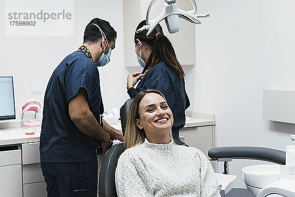 Glückliche junge Frau sitzt auf dem Zahnarztstuhl in der Klinik