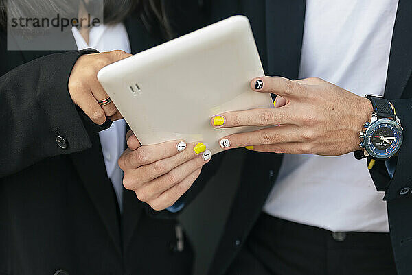 Geschäftsmann mit lackiertem Nagel nutzt Tablet-PC mit Kollege