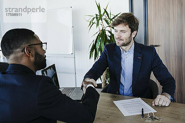 Geschäftsmann schüttelt dem Kunden die Hand  nachdem er im Büro den Vertrag unterzeichnet hat