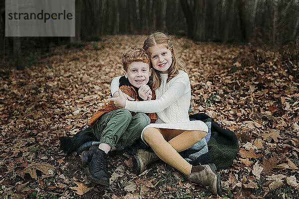 Mädchen umarmt Bruder  der auf Herbstblättern sitzt